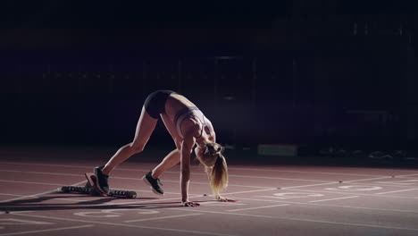 One-woman-in-the-dark-at-the-stadium-is-preparing-to-start-a-race-on-the-track.-Slow-motion-woman-starts-from-hunger-strikes-in-the-stadium-in-the-dark